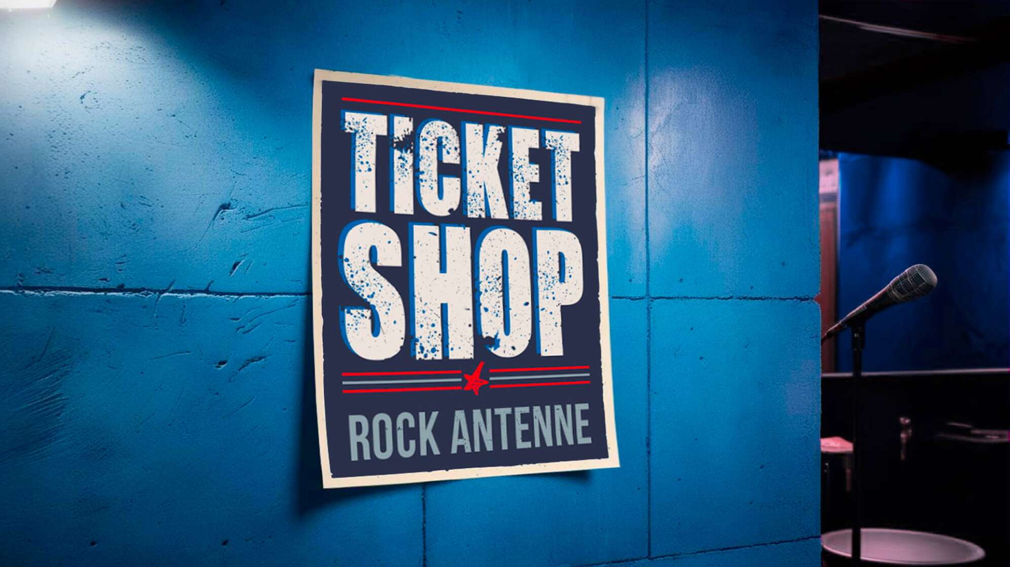 eine bläuliche Betonwand mit einem Plakat, auf dem steht ROCK ANTENNE Ticket Shop