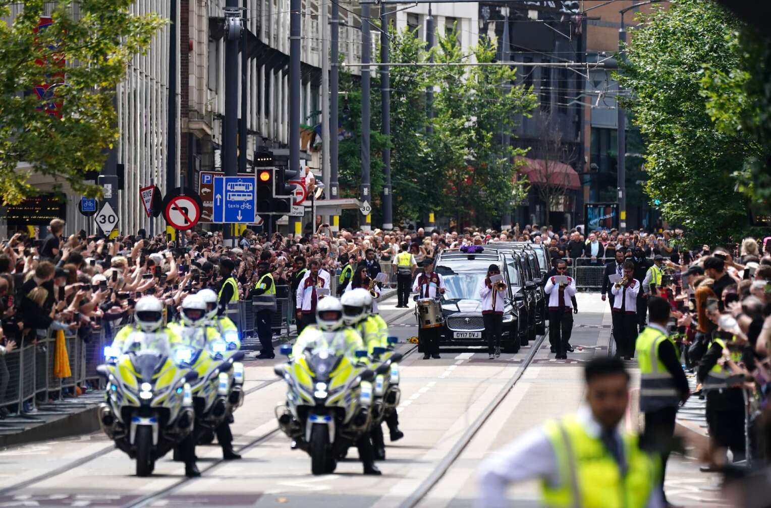 30.07.2025, Großbritannien, Birmingham: Der Trauerzug von Black-Sabbath-Frontmann Ozzy Osbourne fährt die Broad Street entlang, während sein Leichnam nach seinem Tod in der vergangenen Woche im Alter von 76 Jahren in seine Heimatstadt zurückgebracht wird. Foto: Jacob King/PA Wire/dpa +++ dpa-Bildfunk +++
