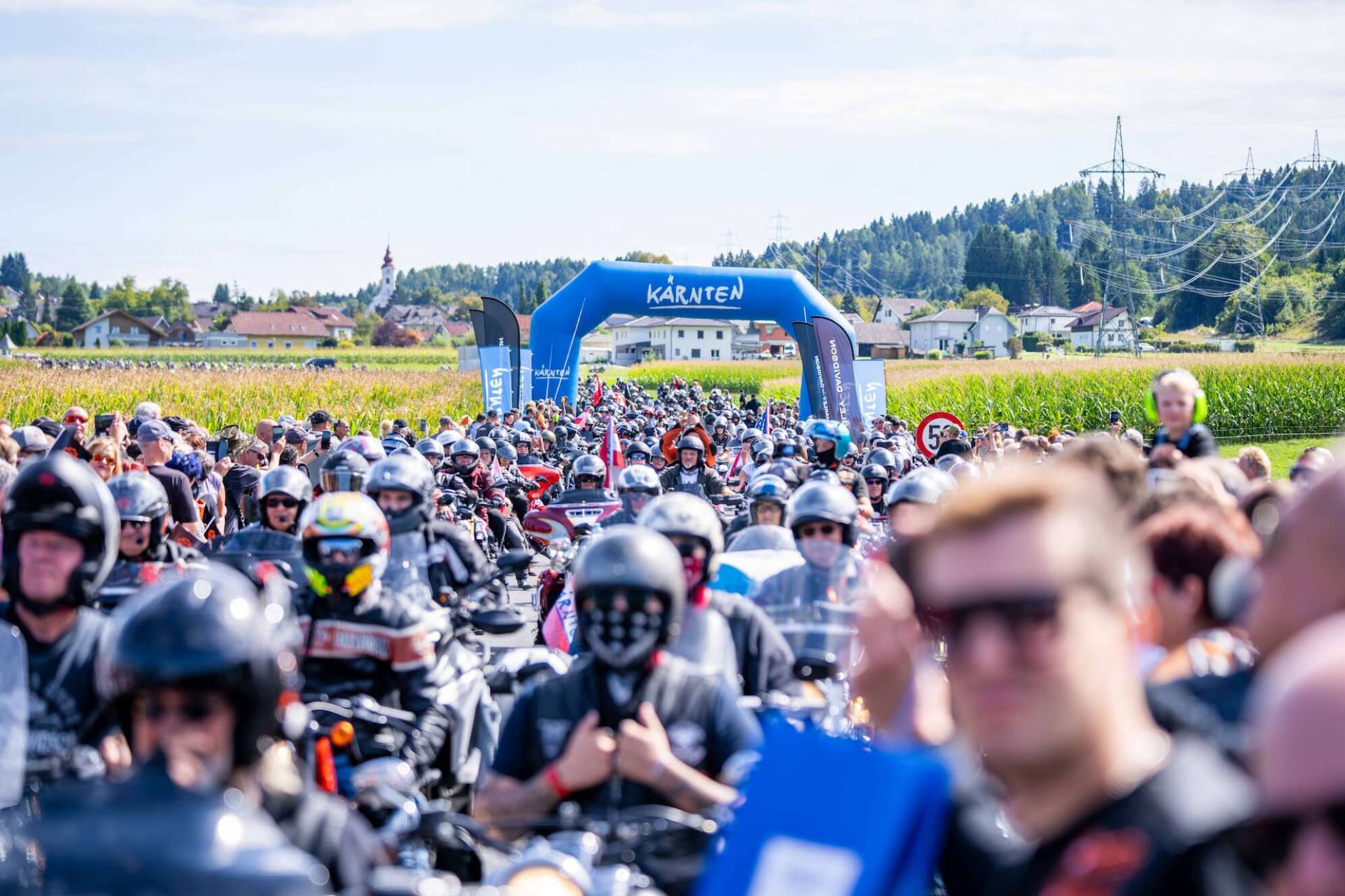 eine Straße voller Biker vor einem aufblasbaren Bogen mit Kärnten-Schriftzug