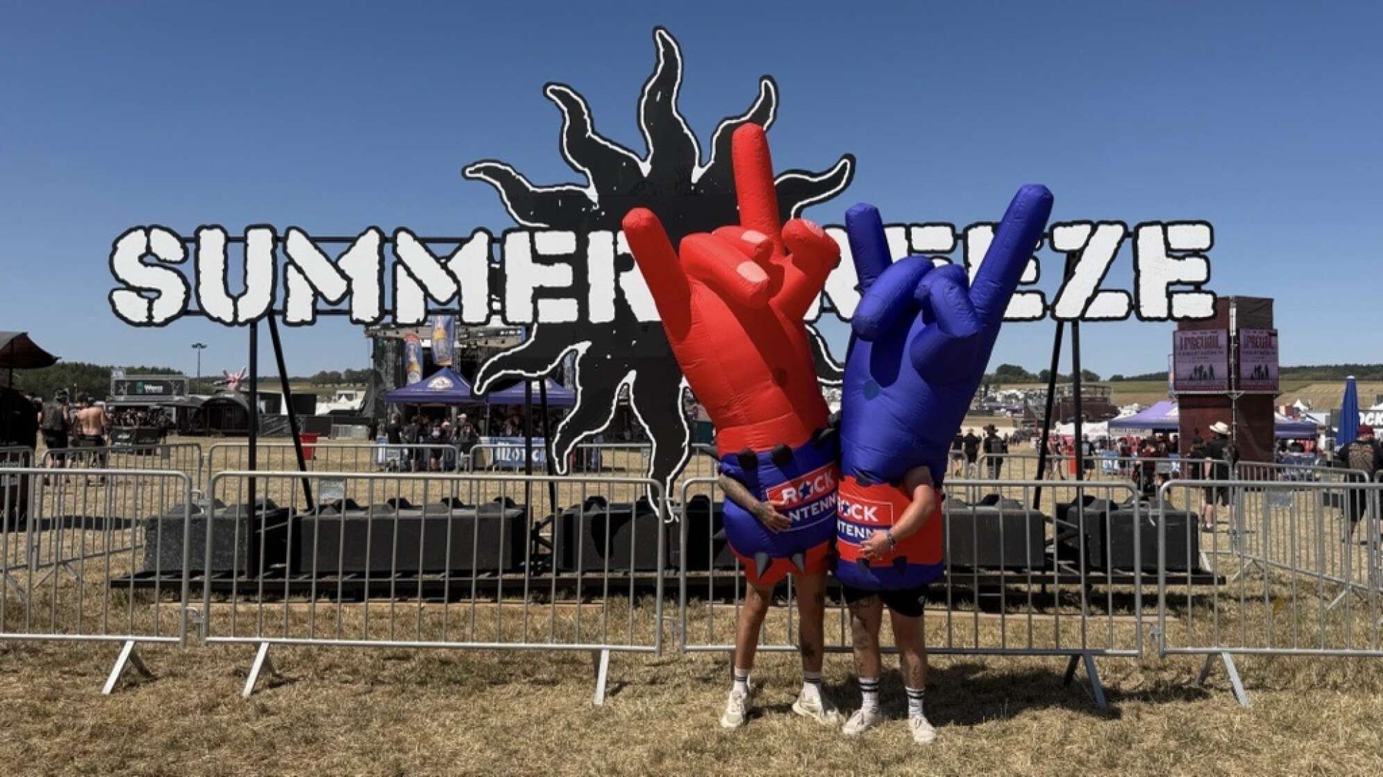 Die aufblasbaren Rockerhand ROCK ANTENNE Maskottchen posieren vor dem Summer Breeze Schild auf dem Festivalgelände
