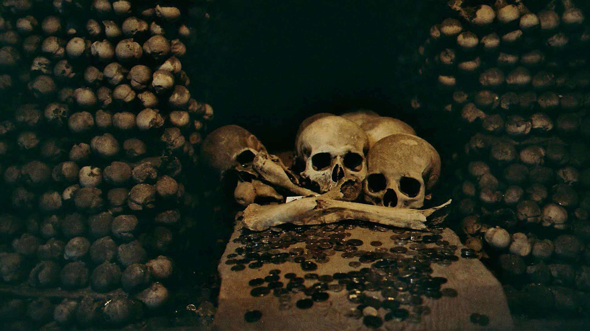 Schädel und Gebeine auf einem Stein, daneben gestapelte Knochen