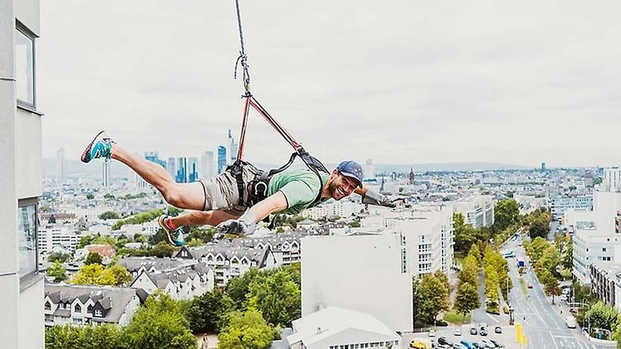 Ein Mann an einem Seil horizontal an einer Hausfassade - er schwebt in der Luft